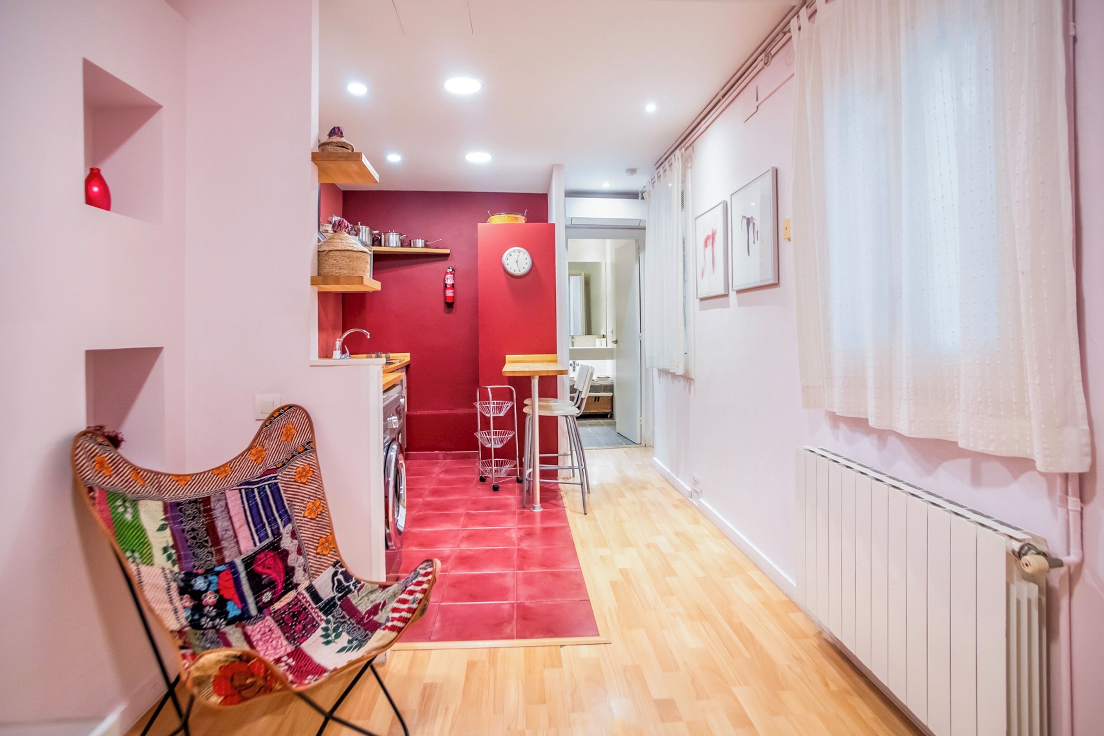 Un pasillo con alfombra roja que conduce a una zona de cocina con un lavamanos, una silla con cojín colorido y un radiador en la pared.