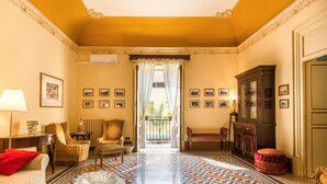 Une pièce avec un sol à motifs, un canapé, des fauteuils, un meuble et une vue par une fenêtre ornée de rideaux.