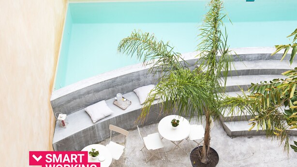 Un espace aménagé au bord de la piscine, avec des sièges disposés en arc de cercle, des tables blanches et des plantes en pot.