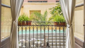 Un balcon donnant sur une piscine, agrémenté de plantes en pot, avec un bâtiment visible au loin.