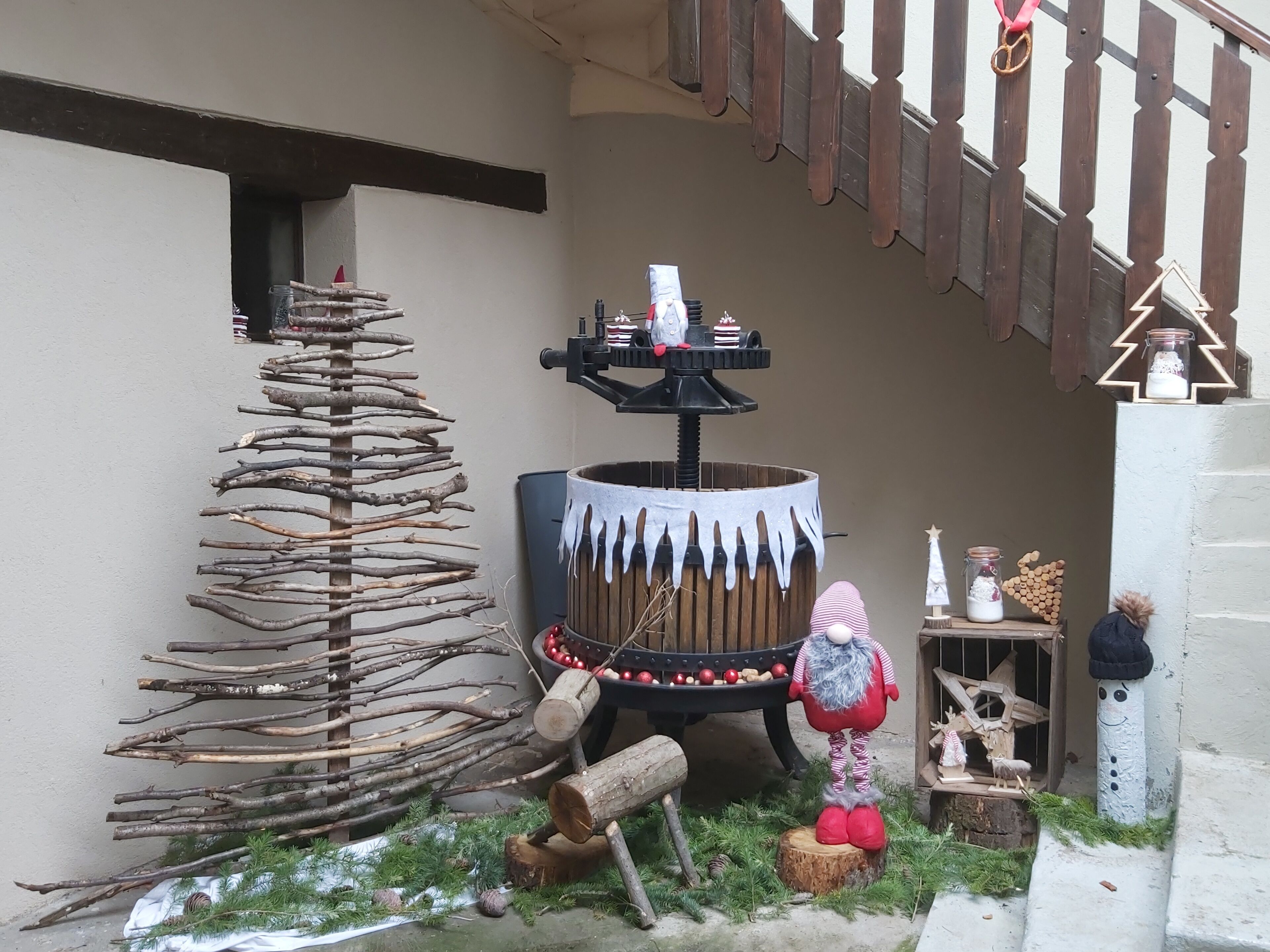 A rustic outdoor setting with a wooden structure resembling a tree, a decorative fountain, and a small Christmas tree display.