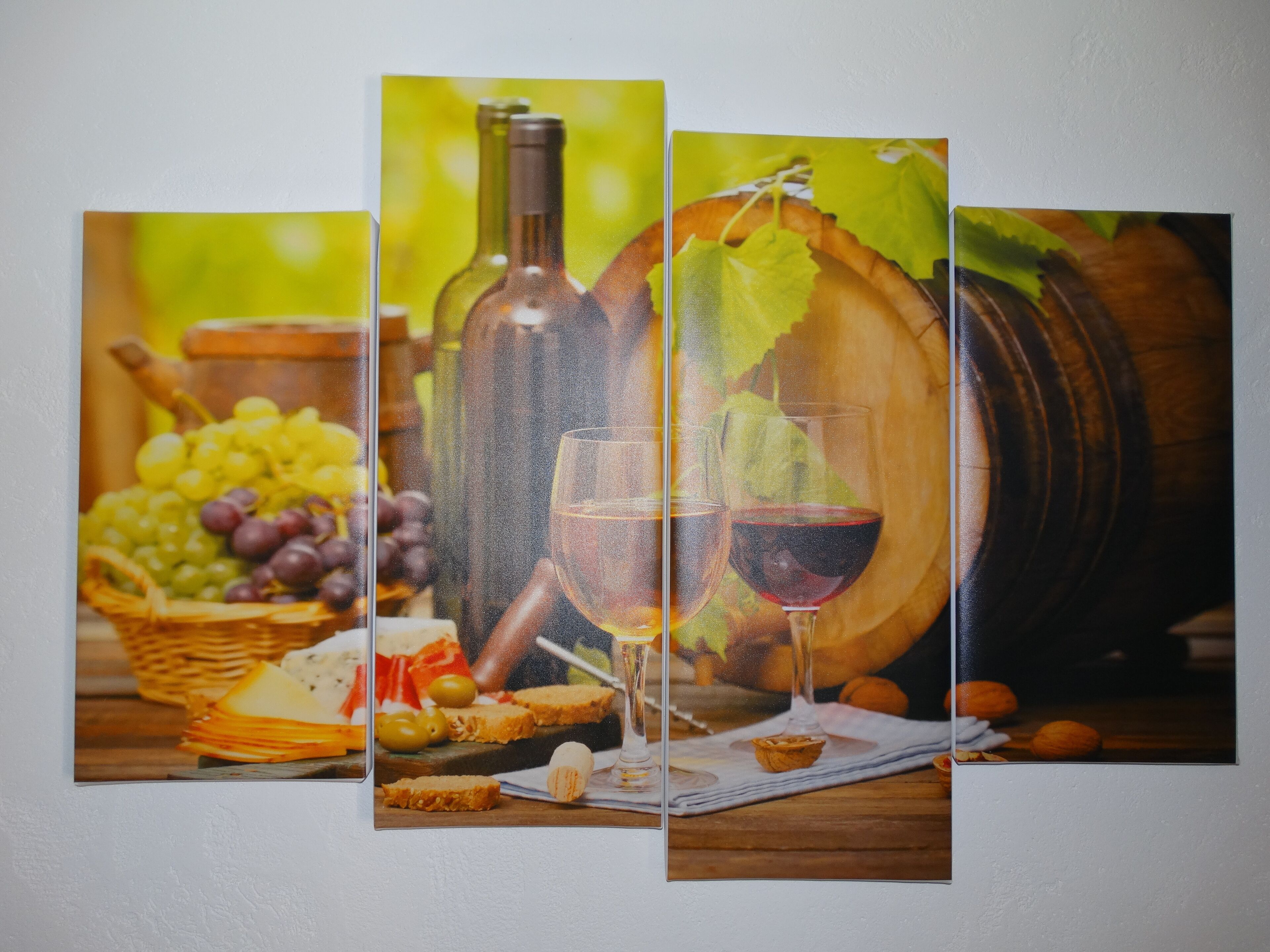 Obra de arte en tres paneles que muestra botellas de vino, copas, uvas, queso y un barril de madera.