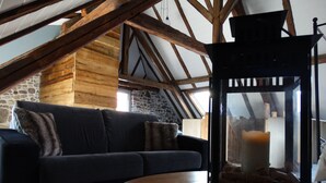 Une pièce chaleureuse de style loft, avec un plafond en bois, un mur en pierre, un canapé bleu foncé et une table ronde en bois.