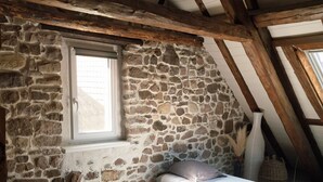 Une chambre avec deux lits, un mur en pierre, une fenêtre et des poutres en bois.