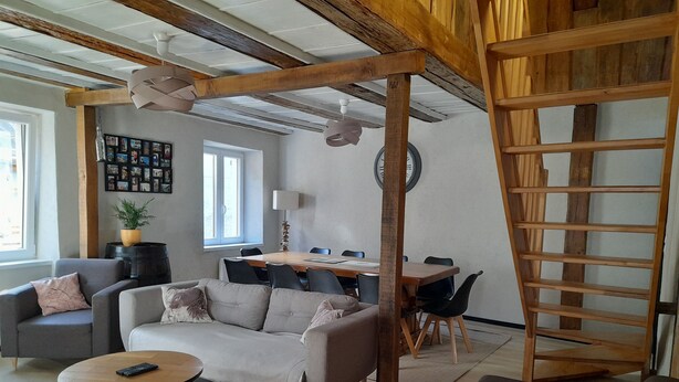 Un salon moderne comprenant un canapé, une table basse, une table à manger avec des chaises, une échelle en bois et un mur orné de photos encadrées.