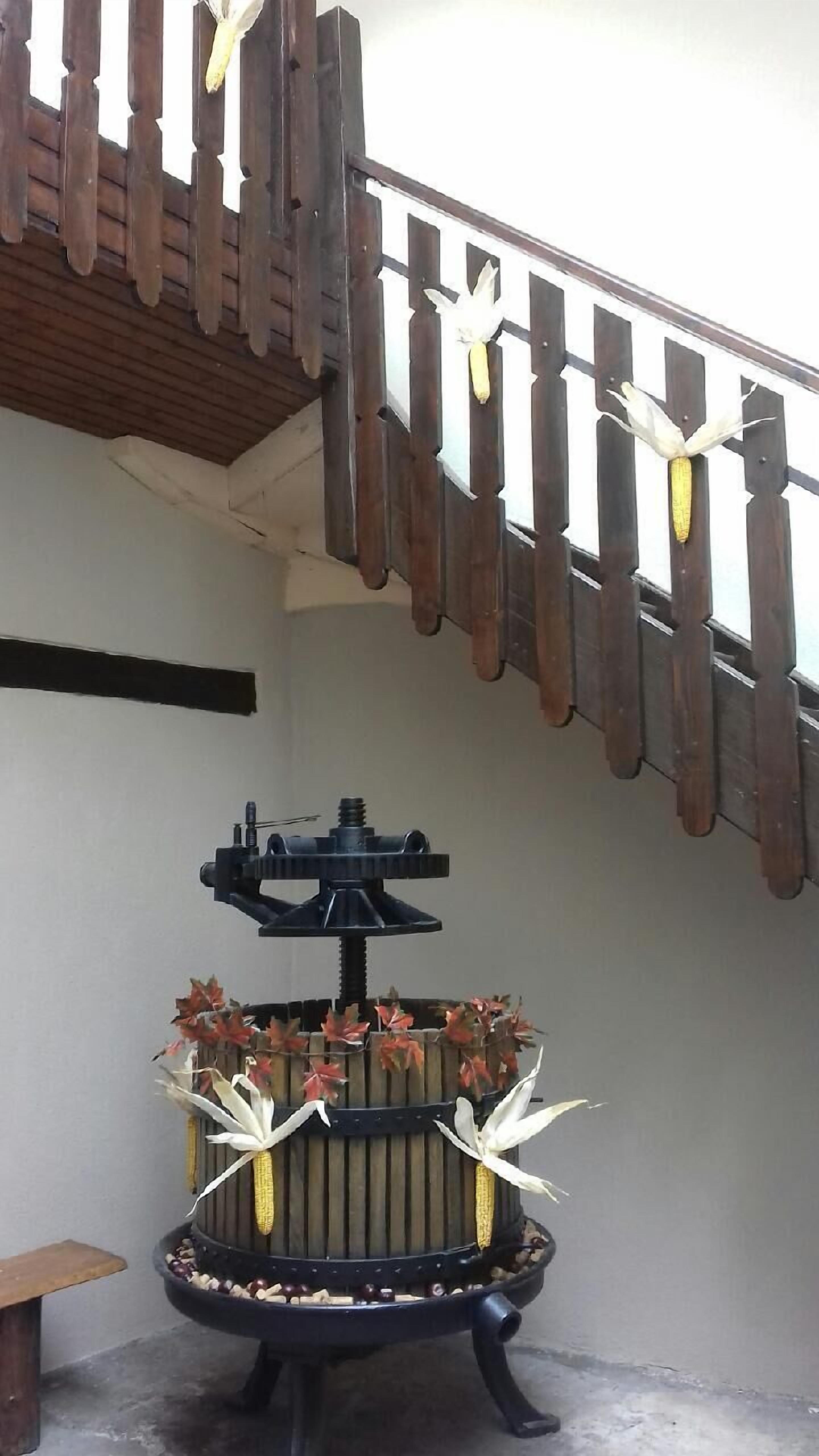 A wooden balcony with a rustic railing and a decorative metal stand with artificial flowers and corn.