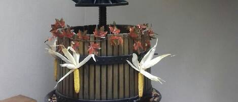 A wooden balcony with a rustic railing and a decorative metal stand with artificial flowers and corn.