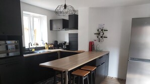 Une cuisine moderne dotée d’un îlot central, de tabourets de bar, d’un four encastré et d’un réfrigérateur en acier inoxydable.