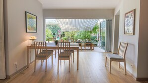 Una habitación amplia con suelo de madera, zona de comedor con mesa y sillas, y un ventanal que ofrece vistas a un jardín.