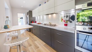 Una cocina moderna con encimera blanca, electrodomésticos de acero inoxidable y un comedor con una silla blanca.