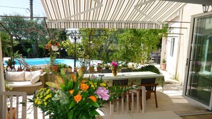 Un patio exterior con piscina, asientos cubiertos y plantas en macetas.
