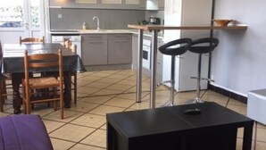 Un espacio habitable compacto con comedor, kitchenette y una pequeña zona de estar con sofá y sillones.