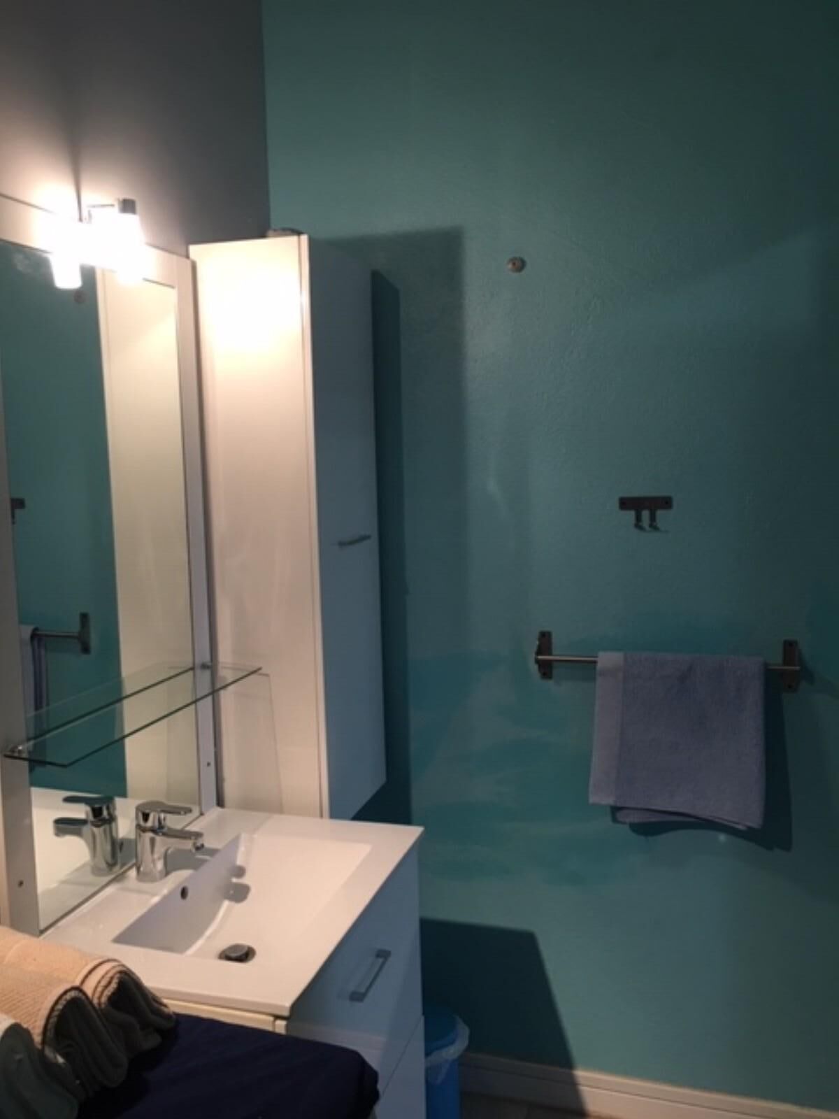 A bathroom with a white sink, a glass shelf, a towel rack, and a mirror.
