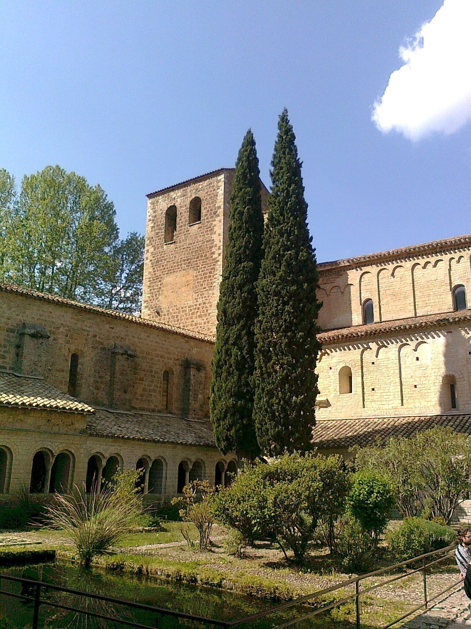 A historic building with a central tower, arched windows, and a courtyard with trees and a small pond.