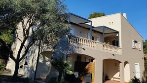 A two-story house with a balcony, a stone wall, and a large tree in the foreground. - Independent apartment in Languedoc villa with panoramic views (Combaillaux)