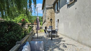 Un patio con suelo de piedra, mobiliario de mimbre y un edificio de piedra con ventanas.