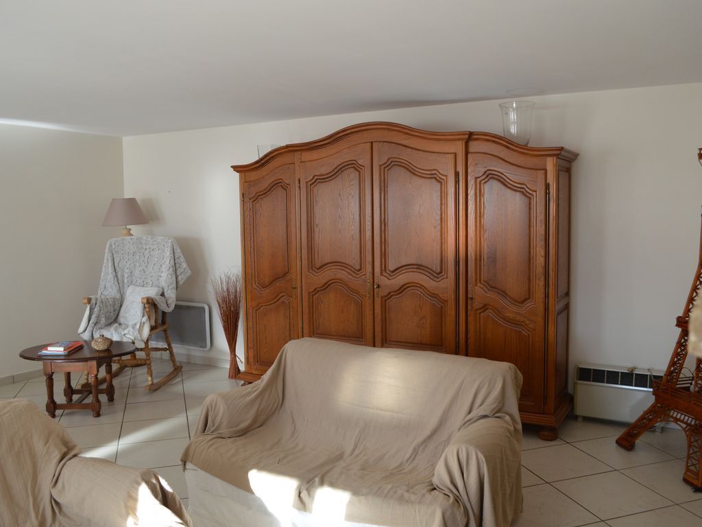 A living room with a beige sofa, a wooden wardrobe, a rocking chair, and a small table with a lamp.
