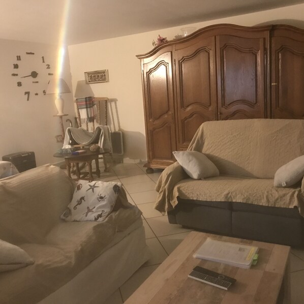 A living room with a sofa, a wooden cabinet, a lamp, and a table with a remote control.