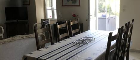 Un comedor con una mesa dispuesta para seis personas, rodeada de sillas de madera. Un televisor está montado en la pared a la izquierda.