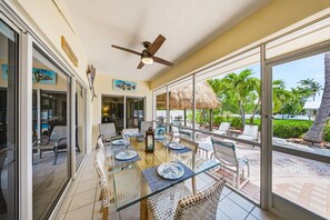 Une terrasse ensoleillée avec une table en verre, des chaises en osier et un ventilateur de plafond.