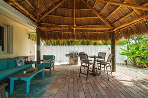 A covered patio with a thatched roof, outdoor furniture, and a grill. - P13 - Loggerhead House 3 Bedroom Home with Private Pool (Key Colony Beach)