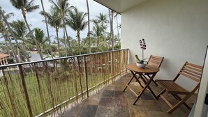 Un balcon avec une table et des chaises en bois, un pot d’orchidée et une vue sur des palmiers et une rue.