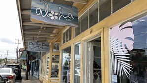 Une devanture de magasin avec une enseigne indiquant « Aloha Boutique » et une autre pour « By The Bay Art, Jewelry & more ».