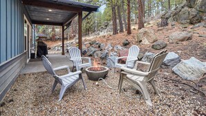 An outdoor seating area with Adirondack chairs and a fire pit, surrounded by a rocky landscape and trees. - Trails End Retreat - Perfect Retreat Luxury Home, Guest Quarters, A/C, Foosball, Ping Pong (Bend)