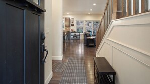 A modern kitchen with a central island, a dining area with a bench, and a view of a forest through large windows. - Trails End Retreat - Perfect Retreat Luxury Home, Guest Quarters, A/C, Foosball, Ping Pong (Bend)