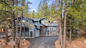A two-story house with a dark exterior, surrounded by pine trees and a stone wall. - Trails End Retreat - Perfect Retreat Luxury Home, Guest Quarters, A/C, Foosball, Ping Pong (Bend)