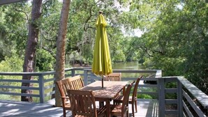 A wooden deck with a table and chairs, a yellow umbrella, and a view of a lake surrounded by trees. - Charming, family friendly and updated kitchen (Kiawah Island)
