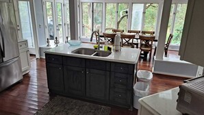 A kitchen with dark cabinets, a double sink, and a large window overlooking greenery. - Charming, family friendly and updated kitchen (Kiawah Island)