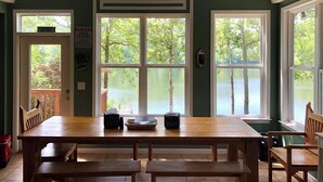 A dining area with a large wooden table and benches, a view of a lake through large windows, and a door with a sign. - Family house by the lake (Shelby)