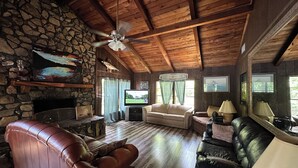 A cozy living room with a stone wall, wooden ceiling, leather sofas, a television, and a fireplace. - Family house by the lake (Shelby)