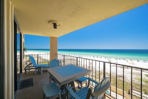 A balcony with a table and chairs, overlooking a beach with umbrellas and people. - Everything is Better at the Beach! ~ Popular One Bedroom @ Phoenix 1 (Orange Beach)