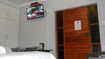 A hotel room with a bed, a television mounted on the wall, a wooden door, and a small table with a kettle.
