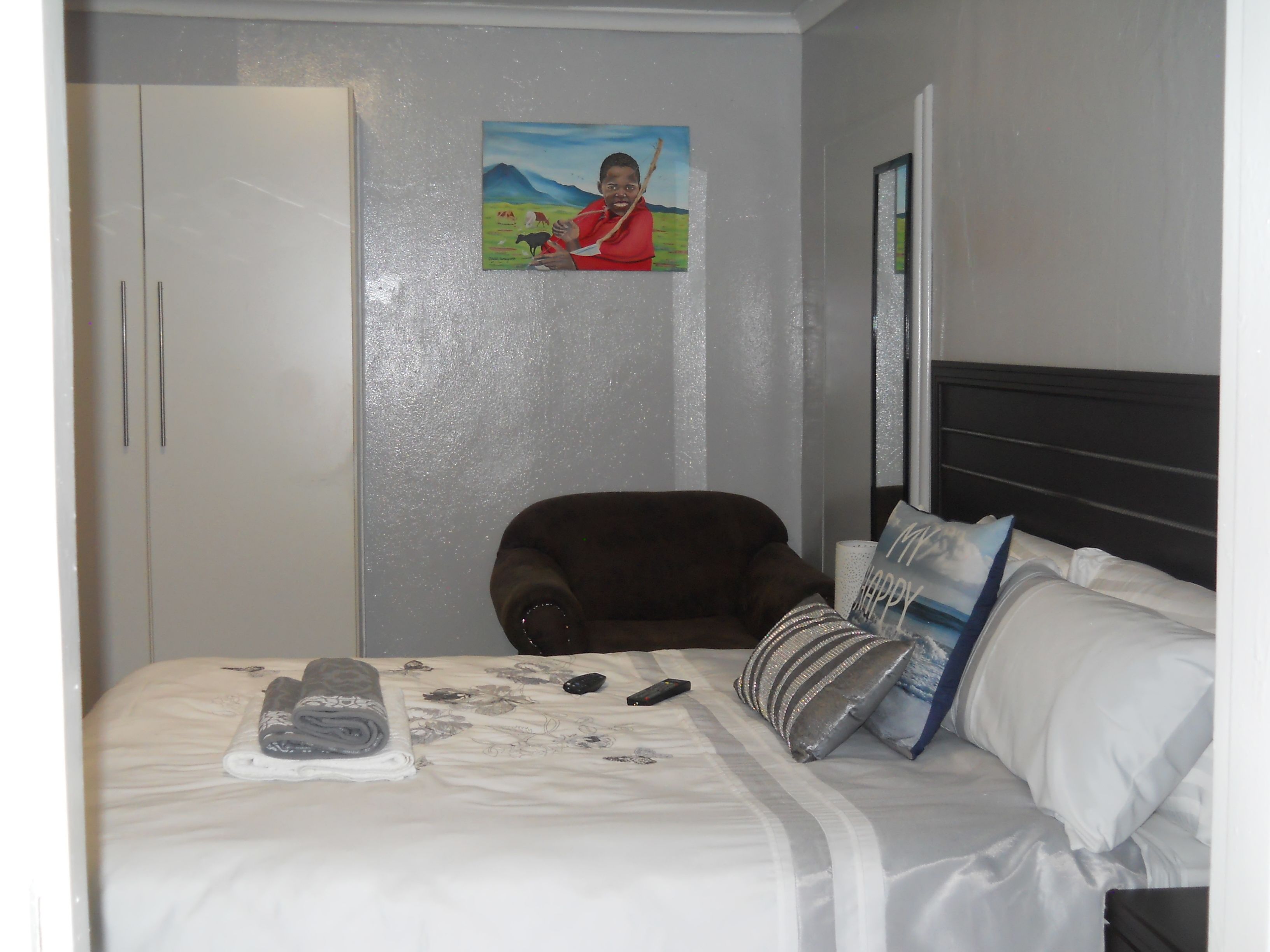 Habitación de hotel con cama, una silla, armario y un cuadro en la pared.