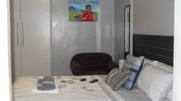 Habitación de hotel con cama, una silla, armario y un cuadro en la pared.