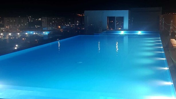 A swimming pool at night with illuminated edges, surrounded by a building with a glass door. - Apartamento Ciudalela NIO (Neiva)