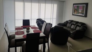 A modern living room with a dining area, featuring a glass table, black leather sofa, and a framed picture on the wall. - Apartamento Ciudalela NIO (Neiva)