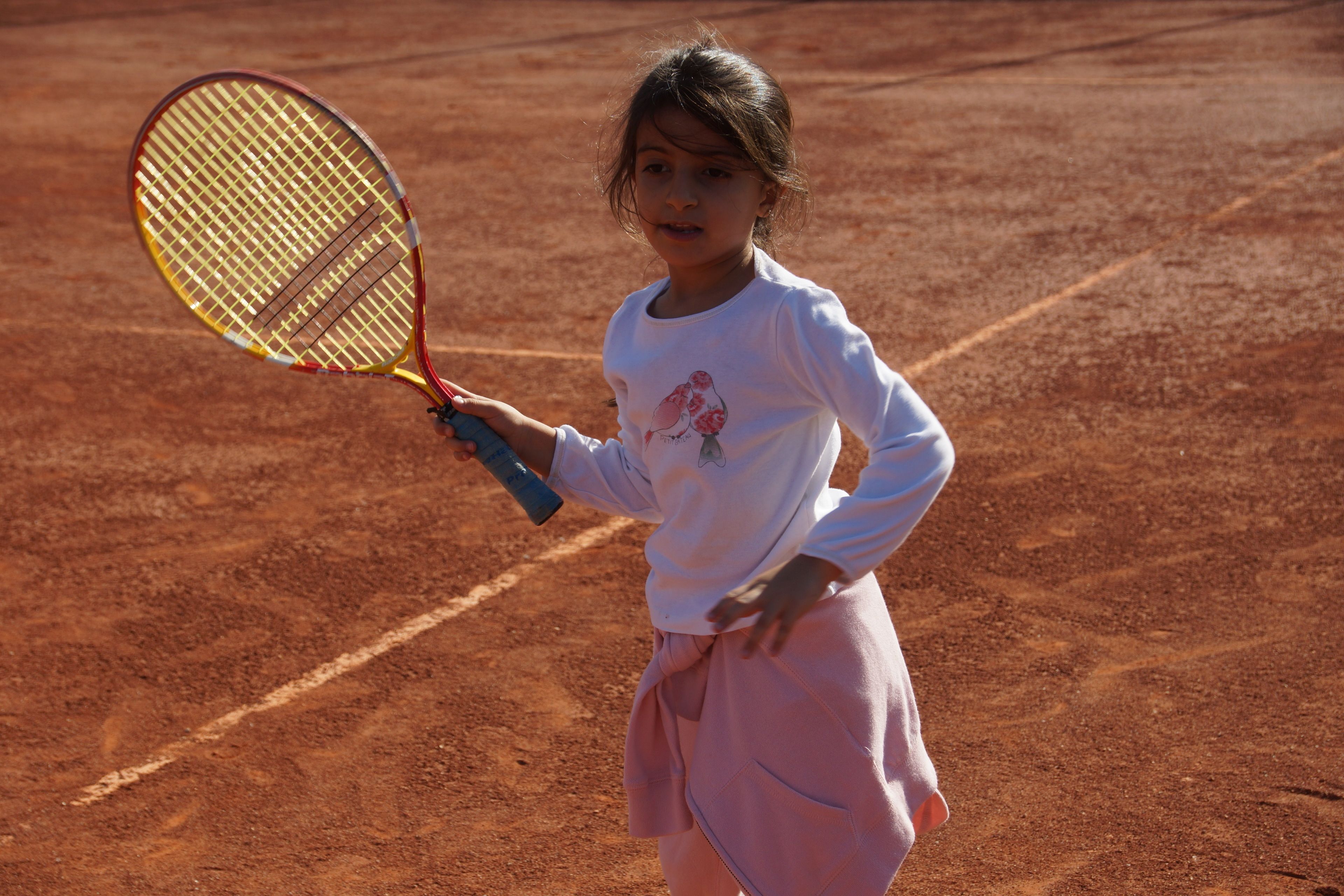 A tennis court with a child holding a tennis racket.