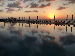 Ein friedlicher Poolbereich mit Liegestühlen und Sonnenschirmen, der den Sonnenuntergang im Wasser widerspiegelt.