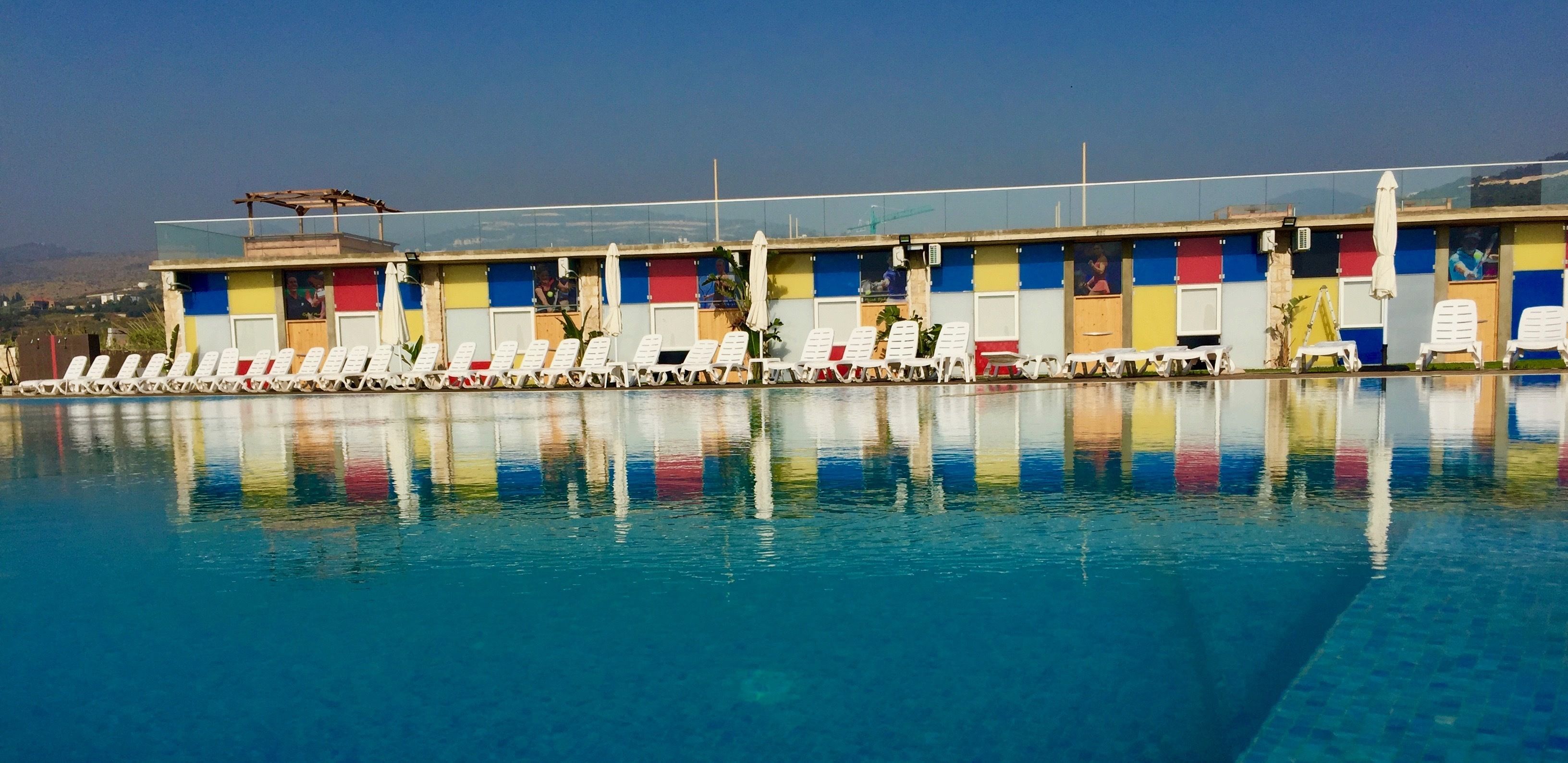 A swimming pool with lounge chairs and colorful changing rooms in the background.