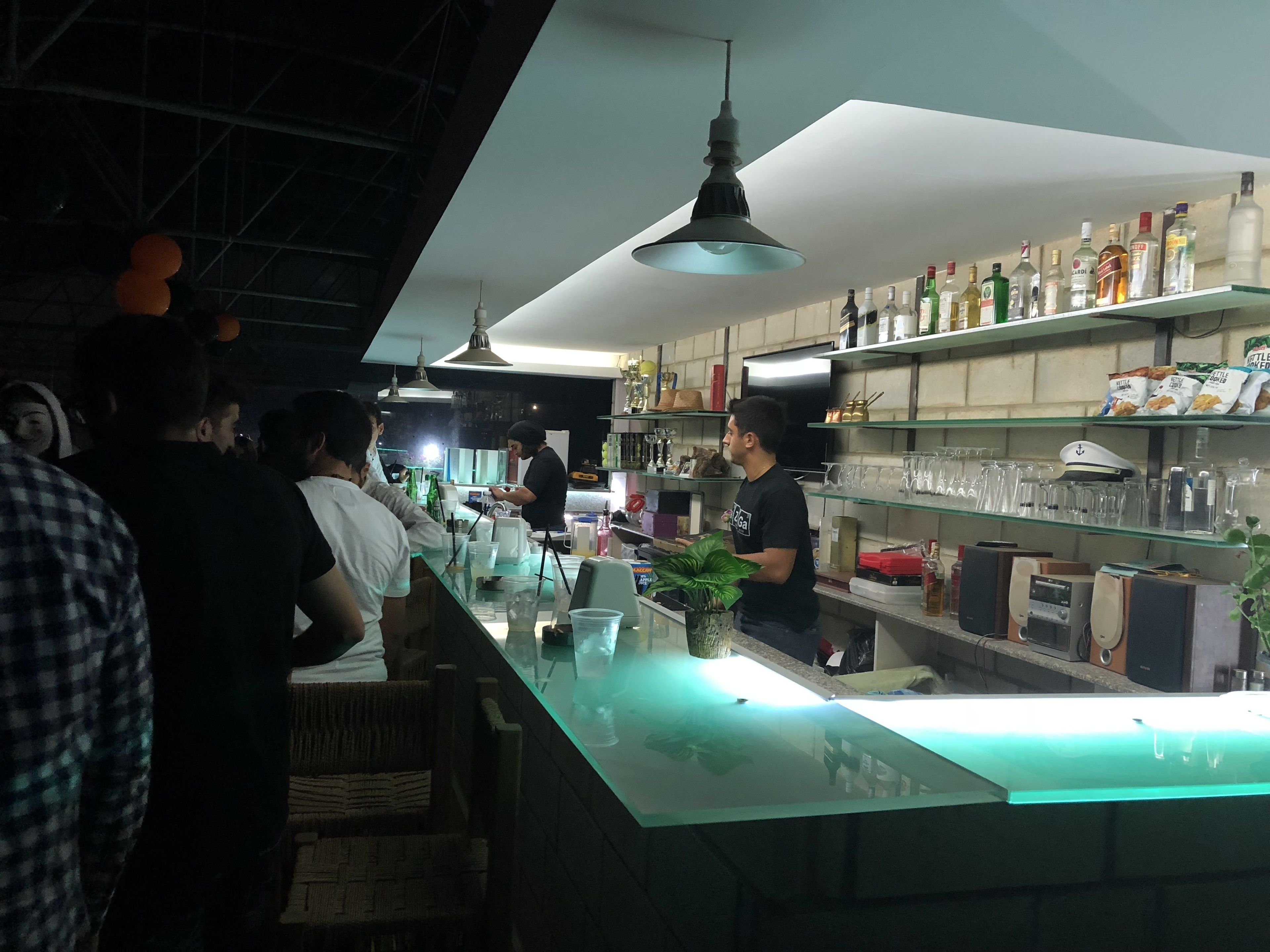 Eine Bar mit einer Theke, Regalen voller Flaschen und einer hängenden Leuchte.