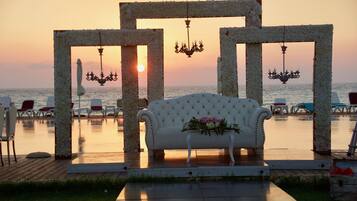 Un sofá blanco con un arreglo floral frente a una vista al atardecer, enmarcada por un arco de flores con candelabros.