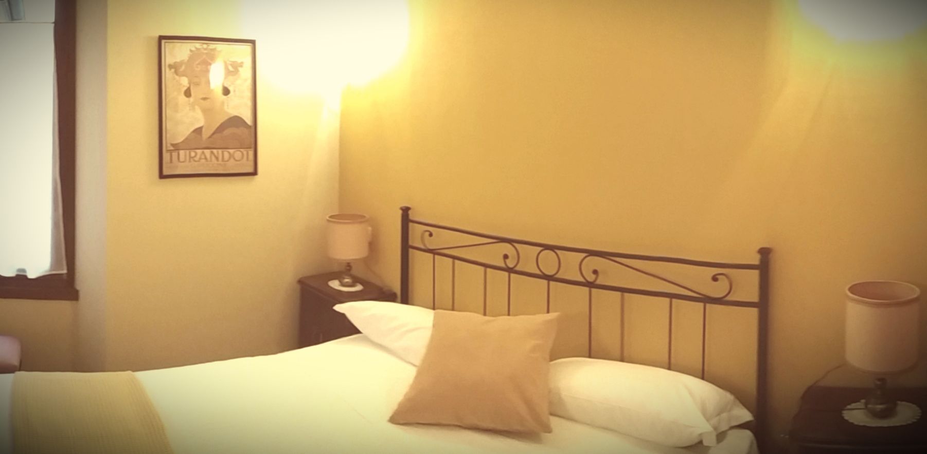 A single bed with a headboard, two bedside tables with lamps, and a framed picture on the wall.