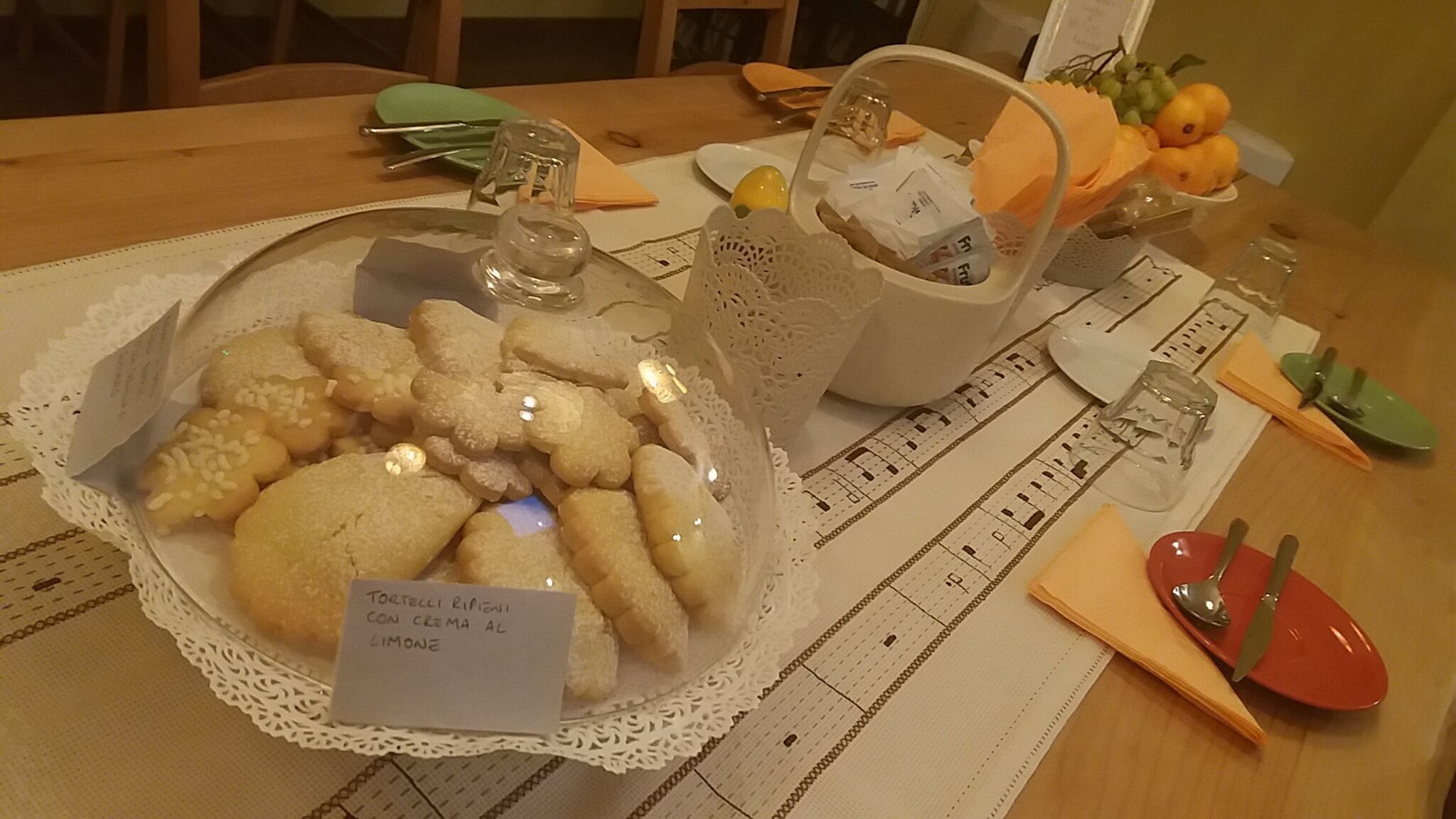 Ein Tisch mit einer transparenten Glasschale, gefüllt mit Keksen, auf denen 'Tortelli Ripieni Con Crema Al Limone' steht.