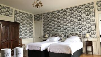 A bedroom with two beds, a chandelier, and patterned wallpaper.