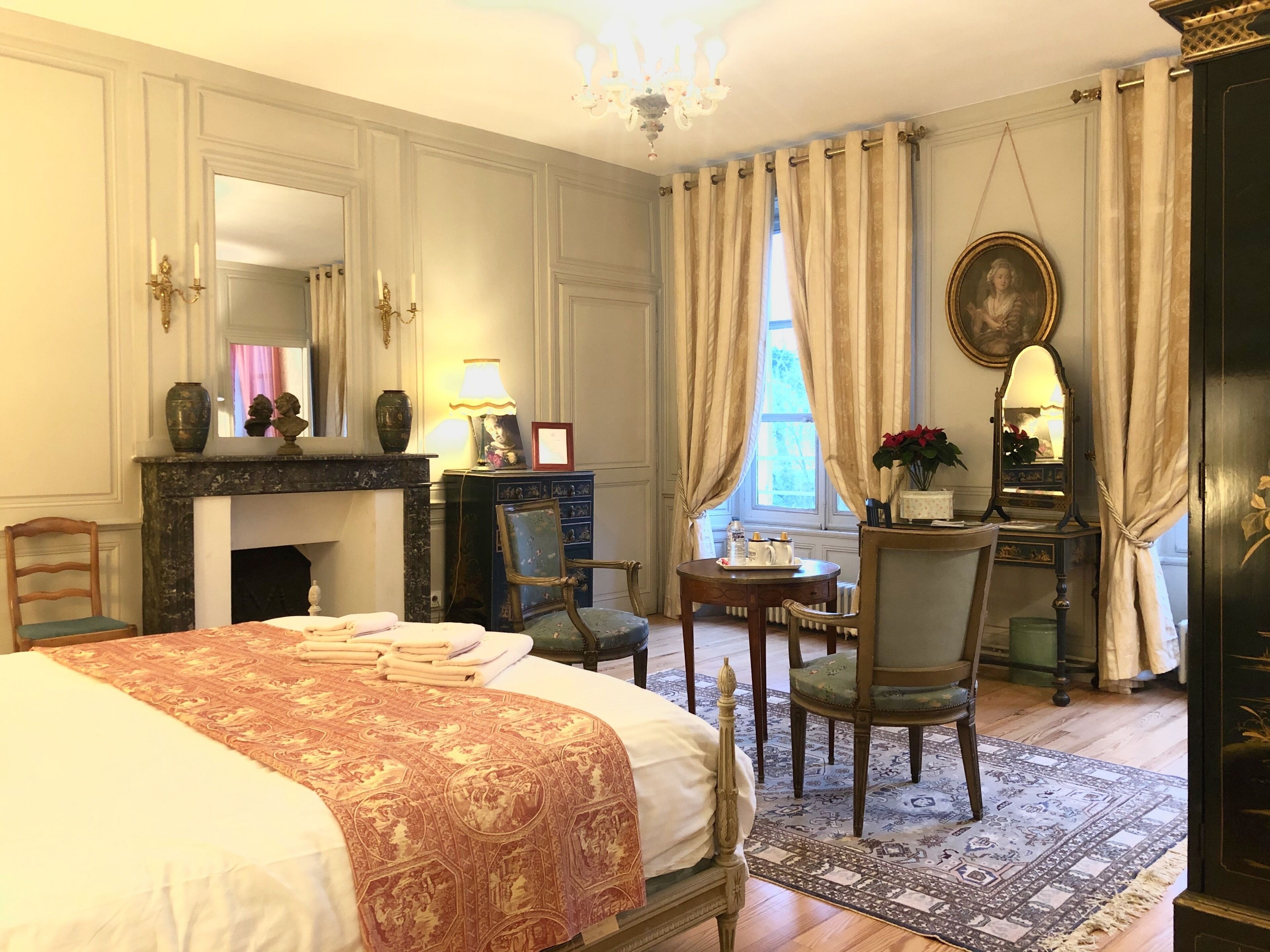 A classic room with a bed, a desk, a chair, a fireplace, and a large mirror.