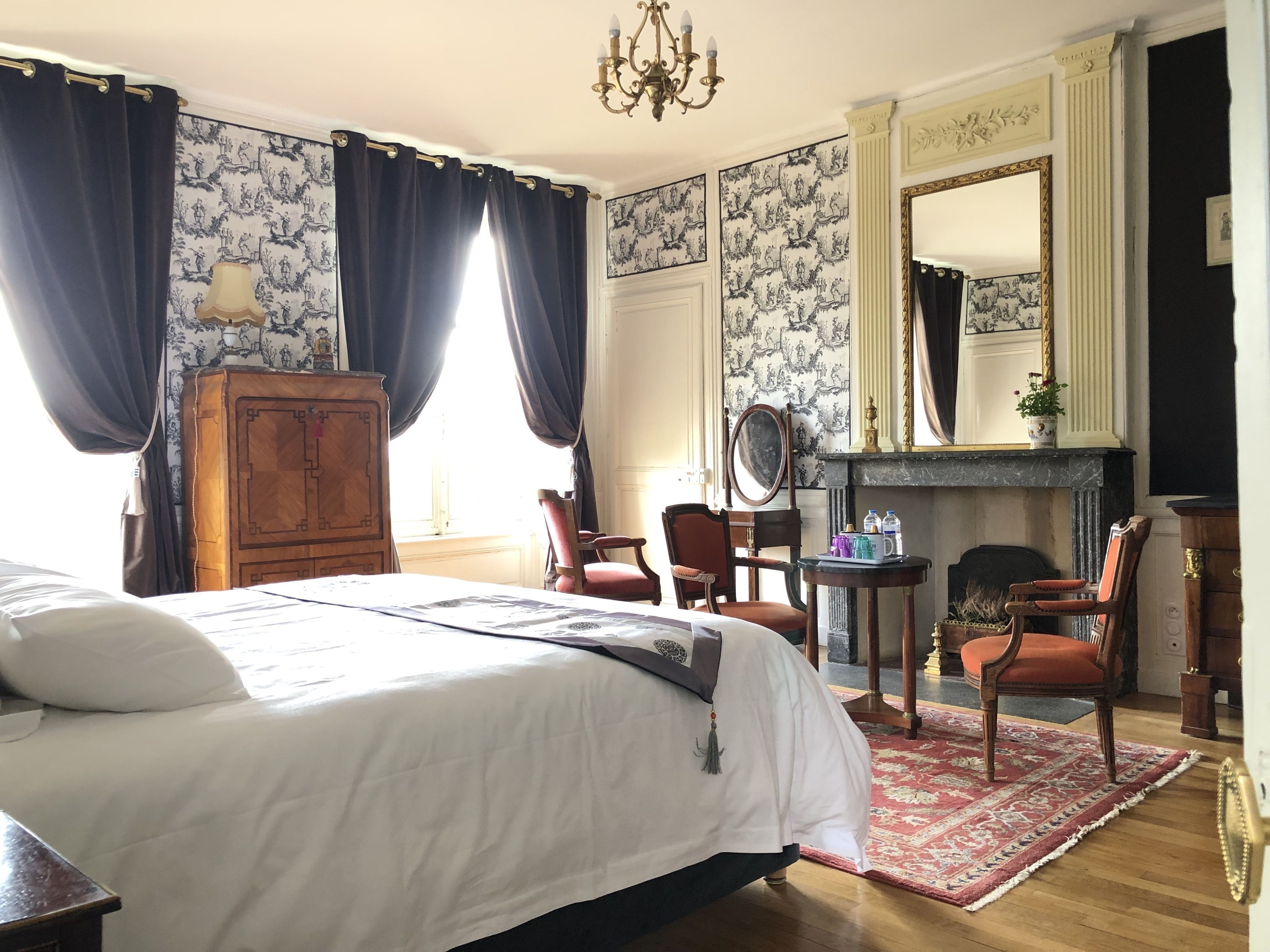 Une chambre à coucher avec un grand lit, une armoire en bois, une cheminée et un miroir.